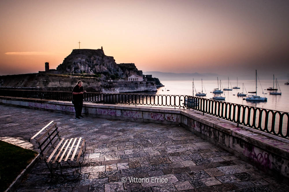 vista sulla fortezza veneziana di corfù all'alba che ritrae una signora e una panchina